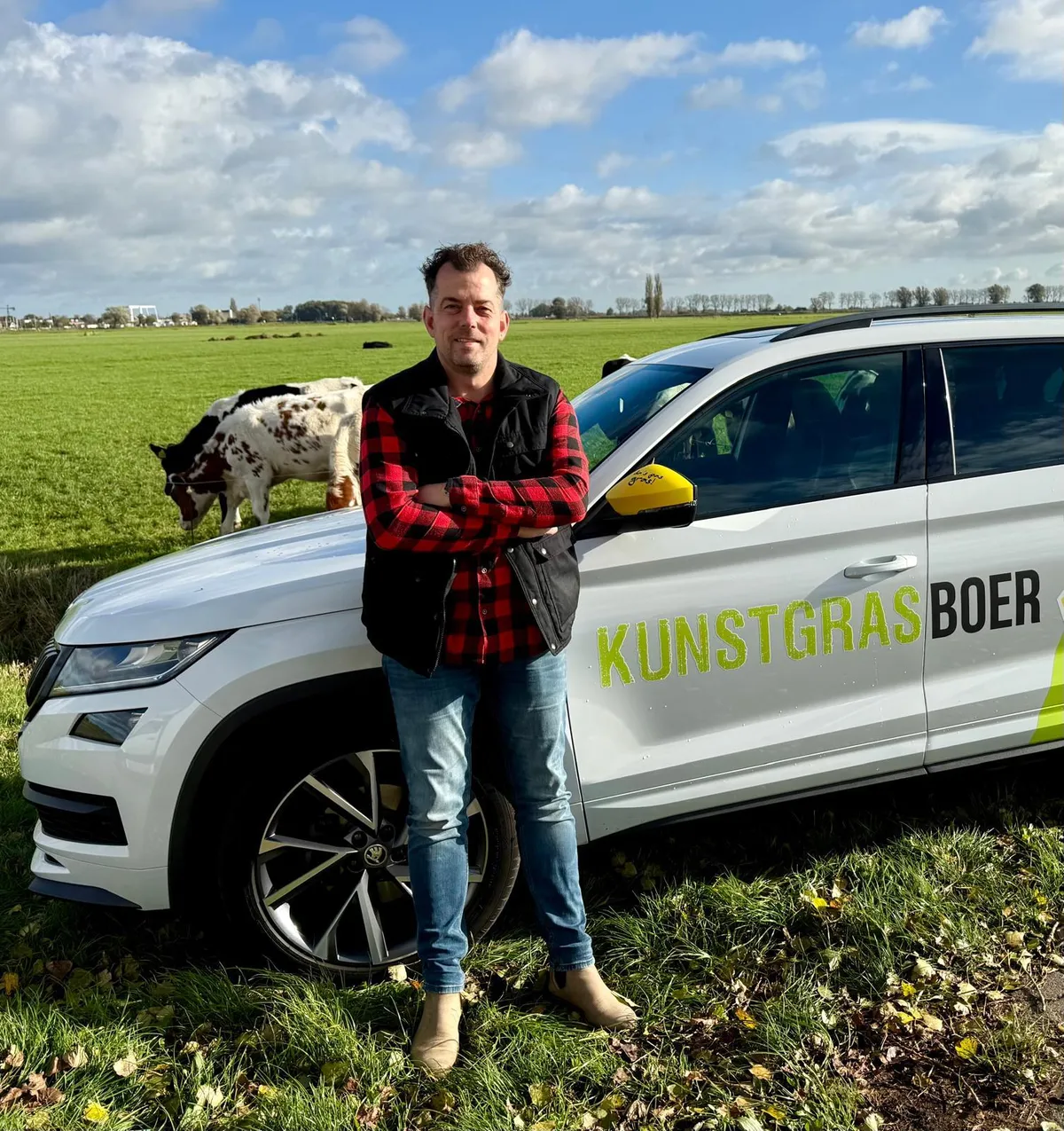 Bauer Henrik von Kunstrasenbauer am Firmenwagen, mit Kühen auf der Weide im Hintergrund