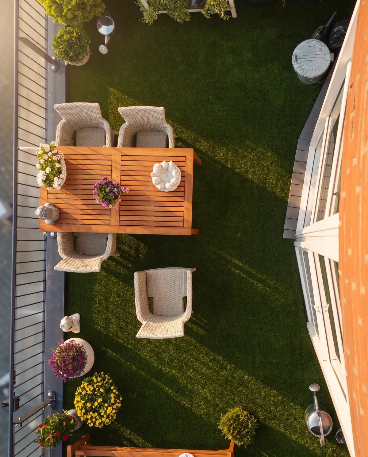 Draufsicht auf einen kompakten Garten mit Kunstrasen, einem Holztisch mit Stühlen und Blumenkästen am Zaun