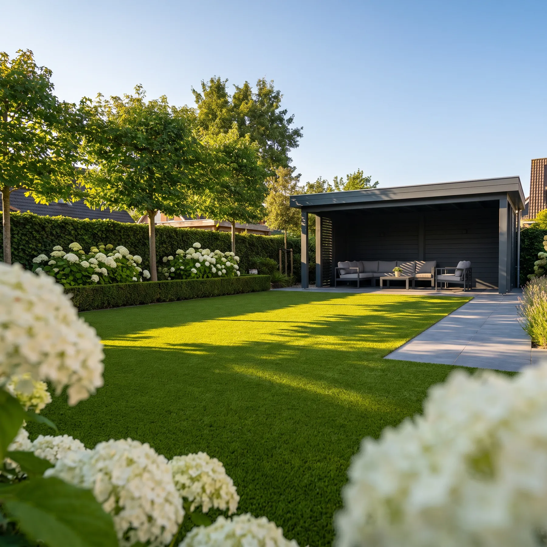 Großzügiger Garten mit gepflegtem Kunstrasen, moderner Überdachung mit Lounge-Möbeln und blühenden Hortensien